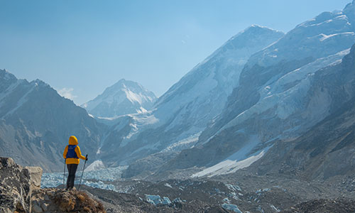 Berglandschaft mit Person mit Wanderstöcken in gelber Jacke